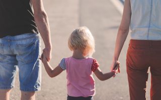 Una famiglia di spalle: due genitori che tengono per mano loro figlio mentre camminano